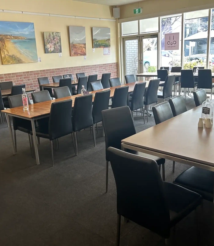 Restaurant dining room with long timber tables and black chairs on a dull floor, before epoxy flooring