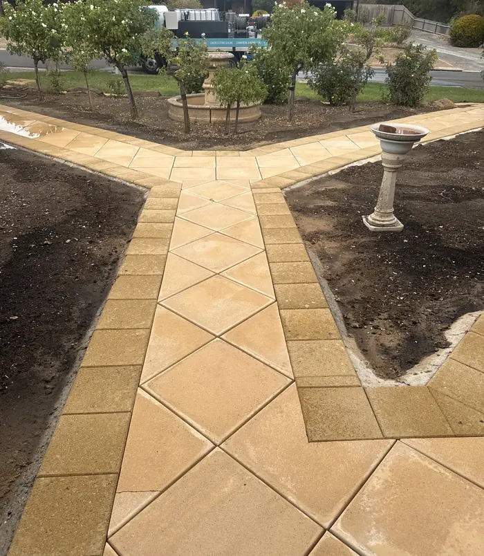 Clean golden paver path forking between garden beds beside bird baths after pressure washing