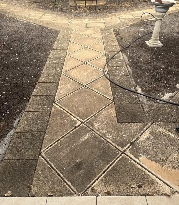 Dull, stained diamond-pattern paver path through a garden, before pressure washing