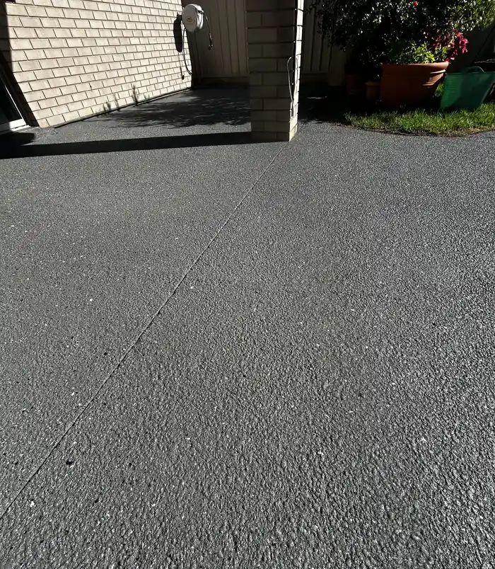 Dark speckled resurfaced concrete beside a brick wall and pot plants