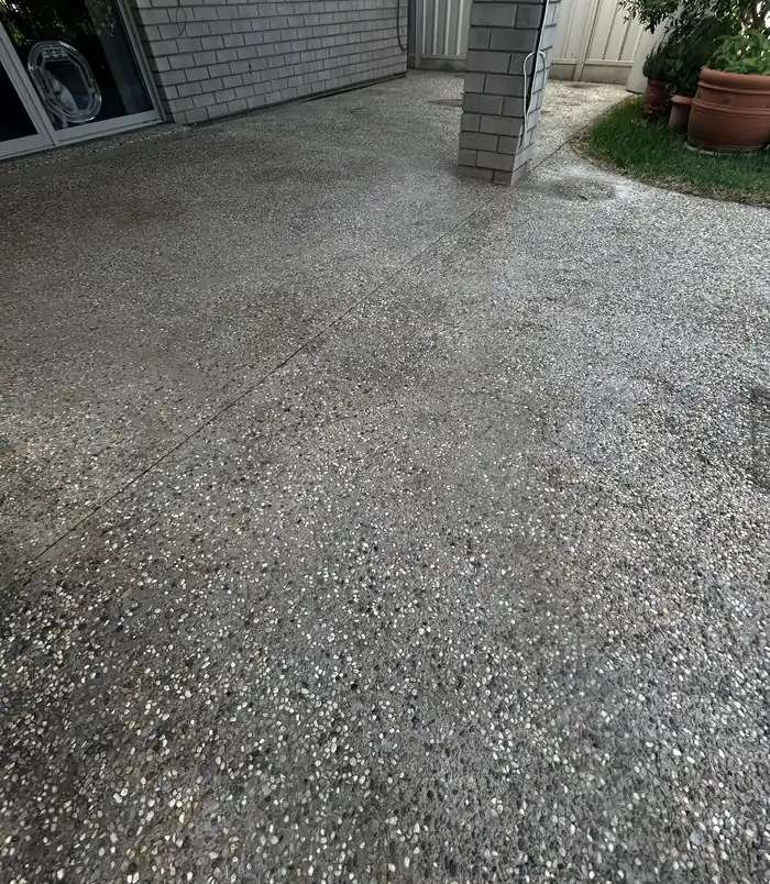 Stained, dull exposed aggregate concrete beside a brick pillar, before concrete resurfacing