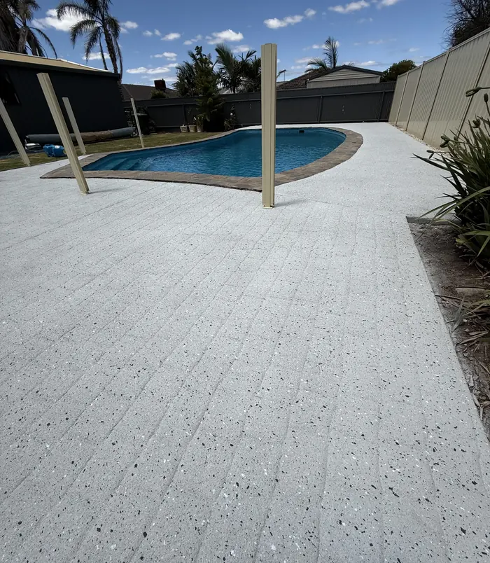 Clean, light resurfaced concrete pool surround beside a swimming pool and fence