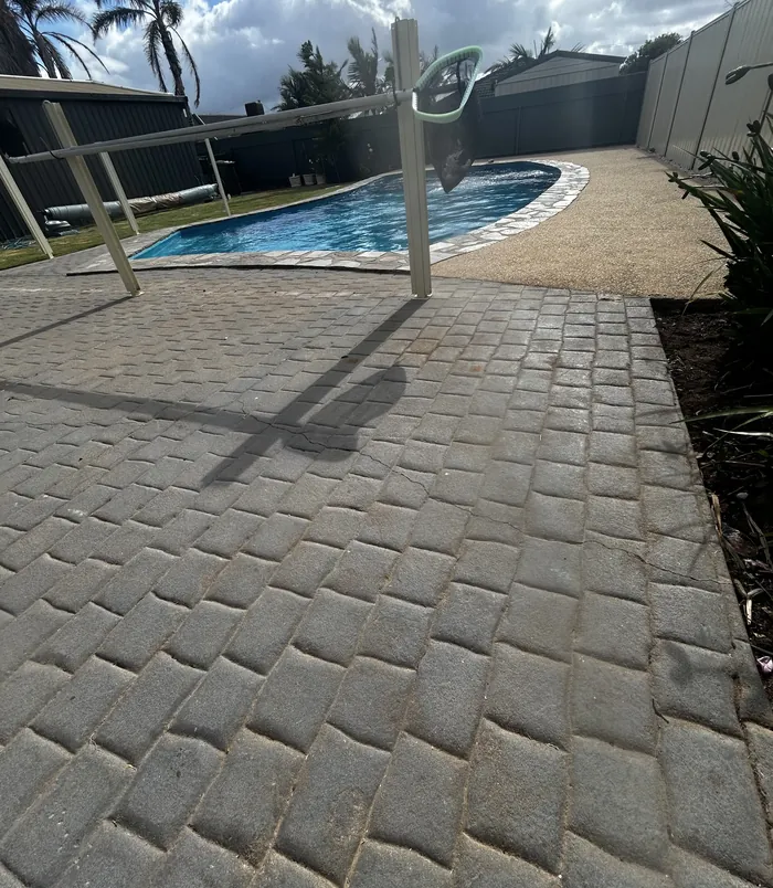 Worn paving around a swimming pool with a safety fence, before concrete resurfacing