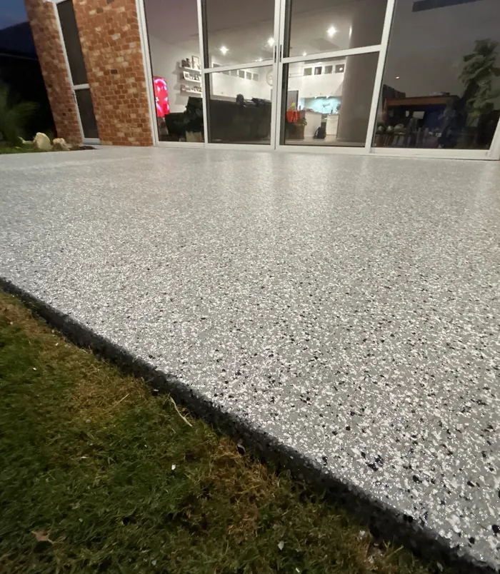 Light grey speckled epoxy flake floor inside a living area beside glass doors