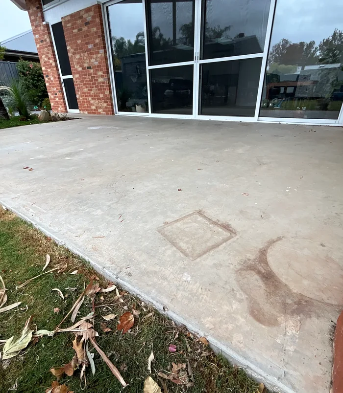 Pale, stained concrete patio outside a brick home with large glass doors, before epoxy flooring