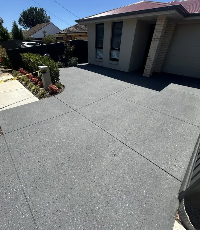 Dark grey resurfaced concrete driveway in front of a modern home with a garden bed