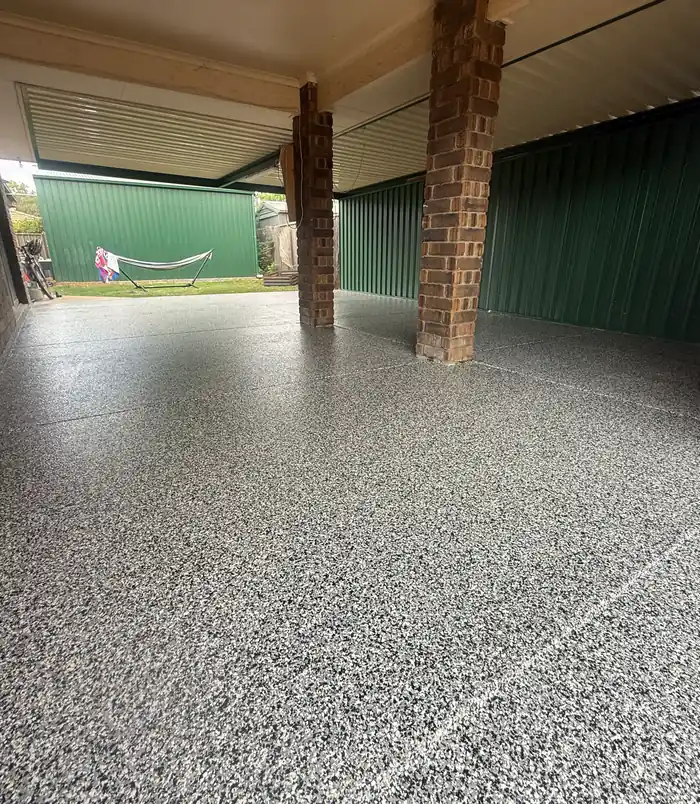 Speckled grey epoxy flake carport floor beside brick pillars and a green shed