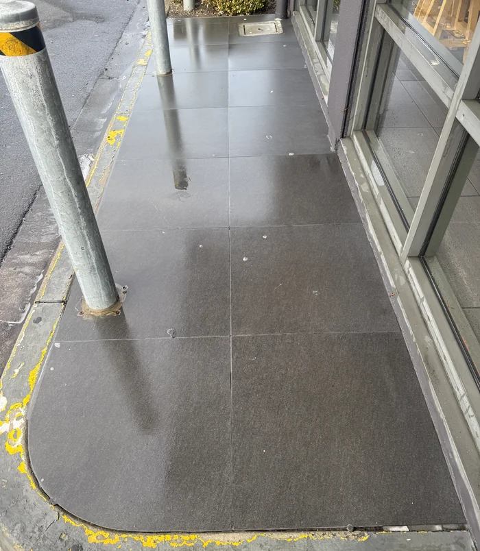 Clean, dark concrete walkway beside a shopfront with steel posts after pressure washing