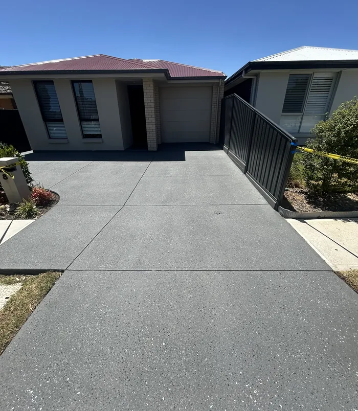 Dark grey resurfaced concrete driveway in front of a brick home with a black gate