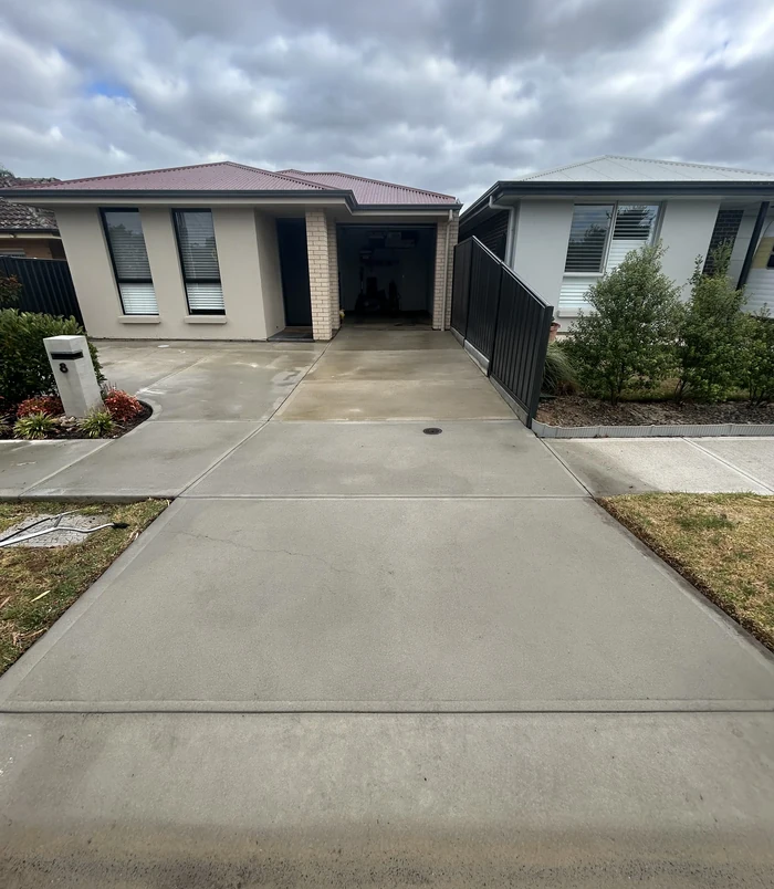 Pale, stained concrete driveway in front of a brick home with a black gate, before resurfacing