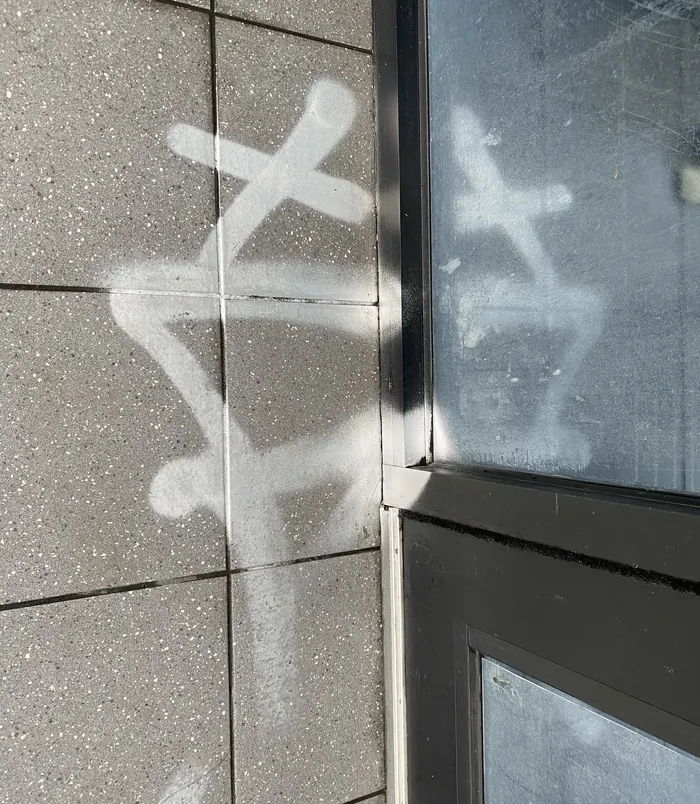 White graffiti tags on a concrete panel wall beside a window, before graffiti removal