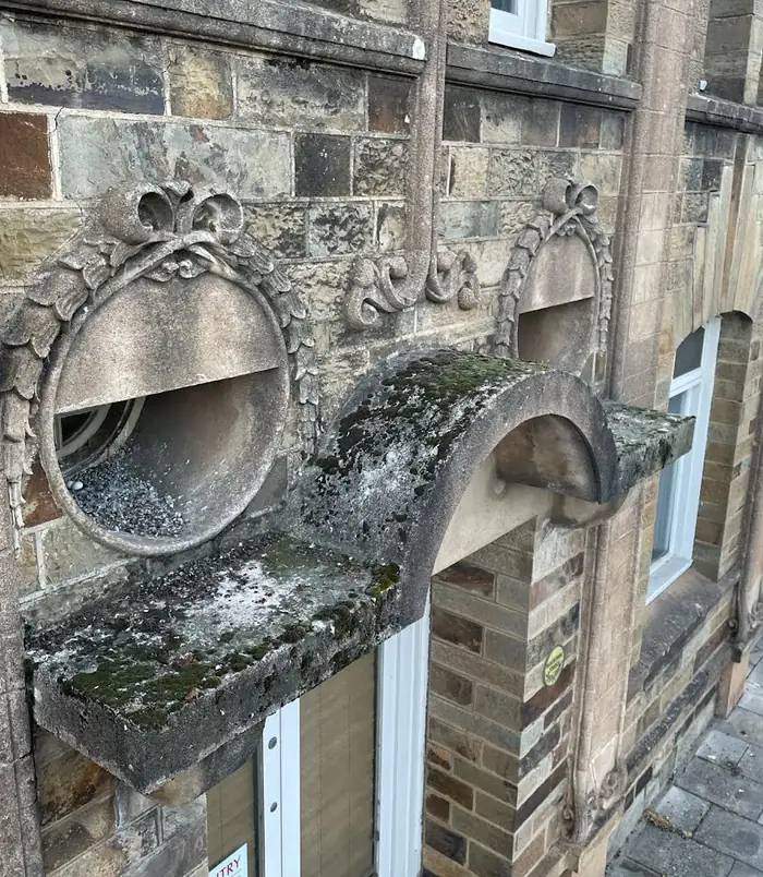 Ornate carved stone detail on a heritage building, dark with grime and weathering, before pressure washing