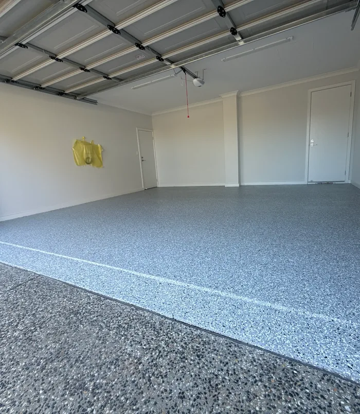 Grey speckled epoxy flake garage floor with white walls and a roller door