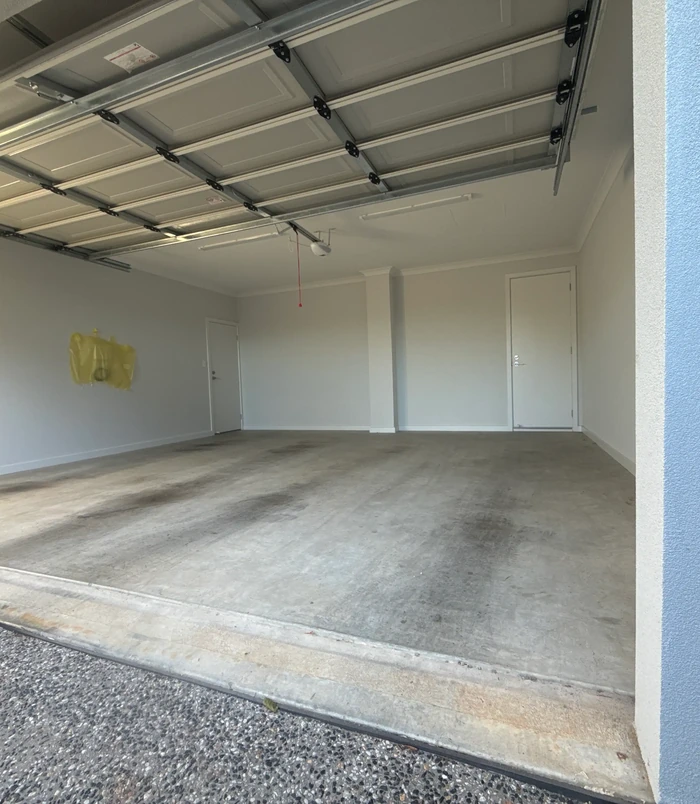 Dull, stained concrete garage floor with white walls and a roller door, before epoxy flooring