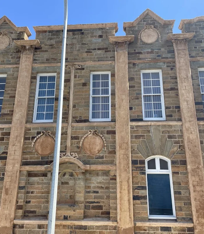 Facade of a heritage sandstone building with clean, golden stone and white-framed windows after pressure washing