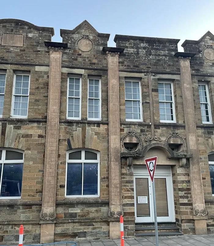 Facade of a heritage sandstone building with dirty, darkened stone and white-framed windows, before pressure washing