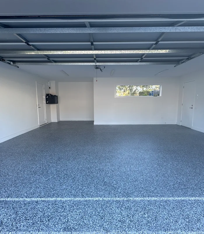 Grey speckled epoxy flake garage floor with white walls and a small window