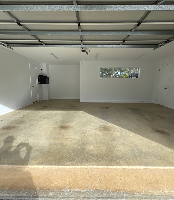 Bare concrete garage floor with white walls and a small window, before epoxy flooring