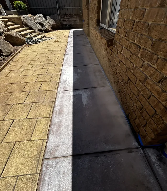 Dull concrete strip between golden pavers and a brick wall, before concrete resurfacing