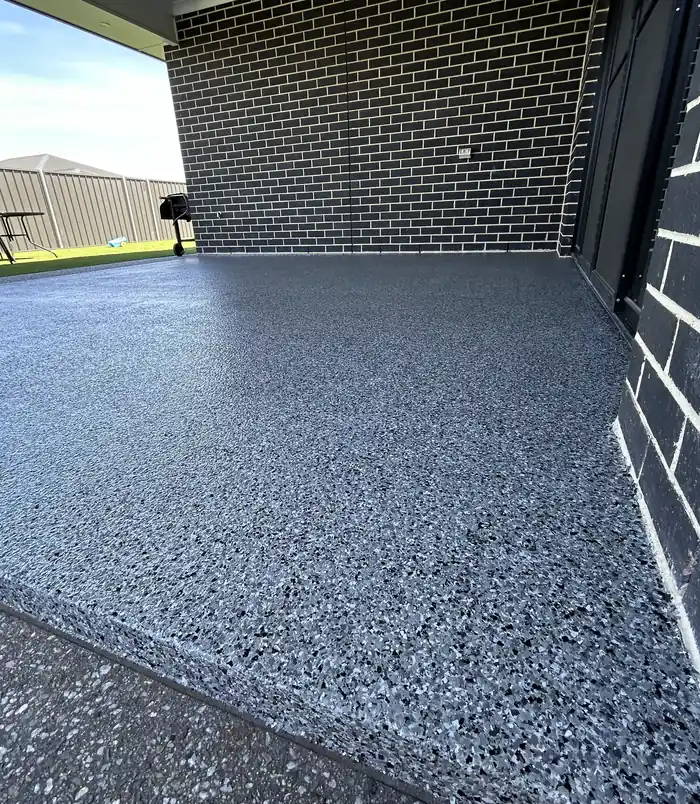 Blue-grey speckled epoxy flake floor beside a dark brick wall