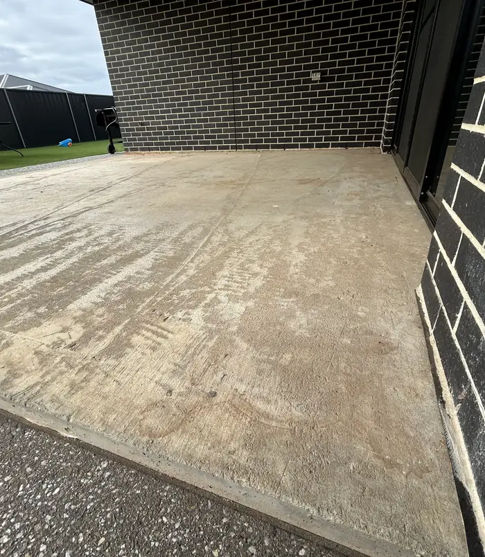 Rough, weathered concrete floor beside a dark brick wall, before epoxy flooring