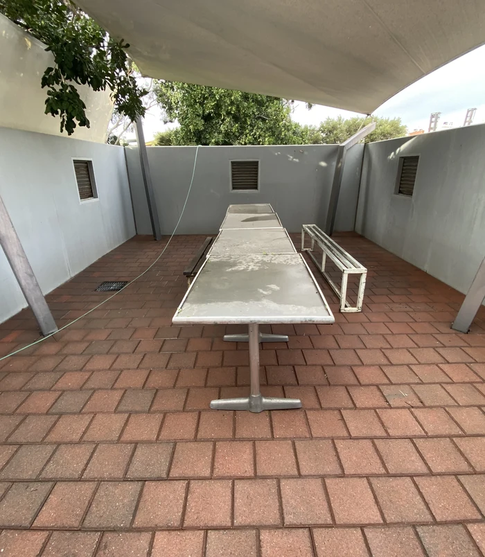 Clean, rich-toned pavers in a shade-sail courtyard with a long outdoor table after pressure washing