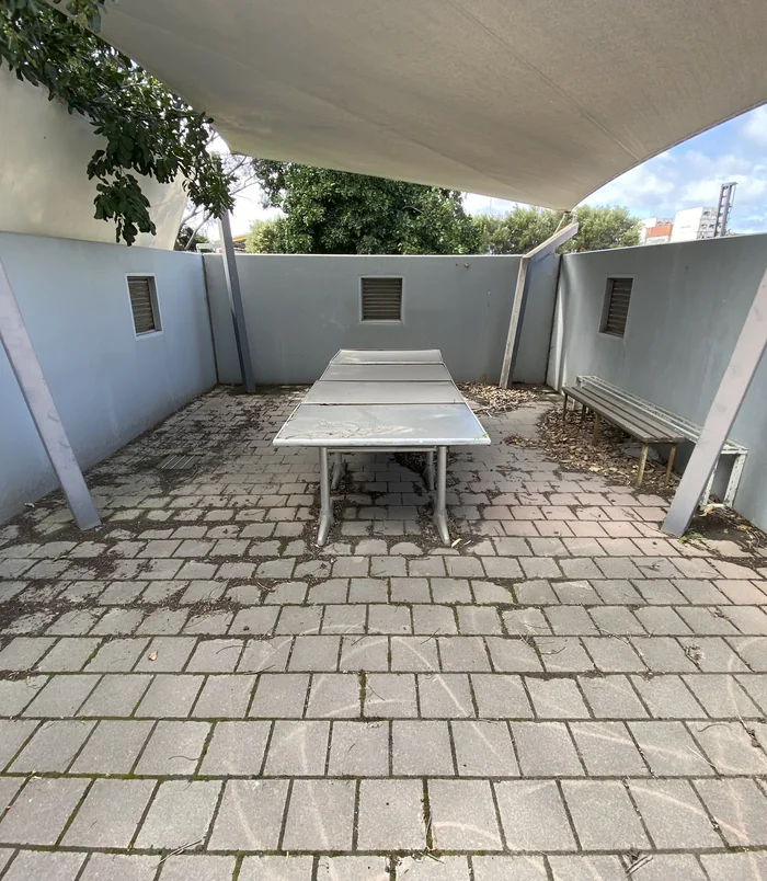 Dirty, discoloured pavers in a shade-sail courtyard with a long outdoor table, before pressure washing