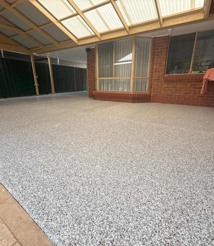 Speckled grey epoxy flake patio floor under a pergola beside a brick wall
