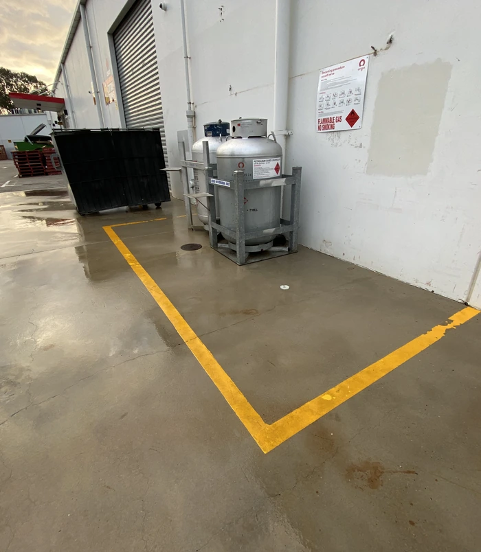 Clean commercial concrete floor around a stainless steel tank with yellow line markings after pressure washing