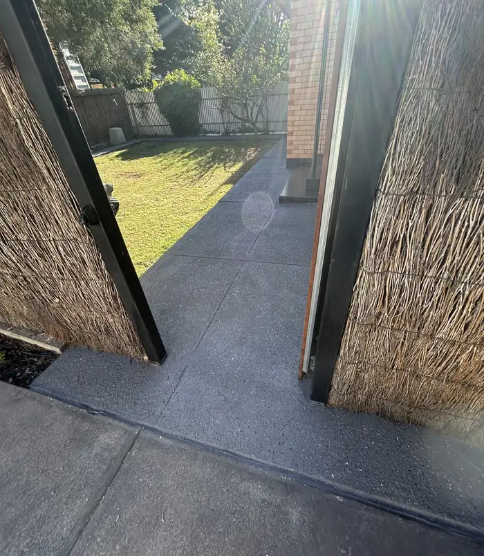 Dark grey resurfaced concrete side path between a woven brush fence and a gate