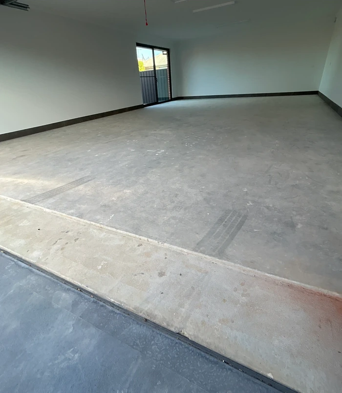 Bare concrete floor in an empty room with a dull, patchy surface, before epoxy flooring