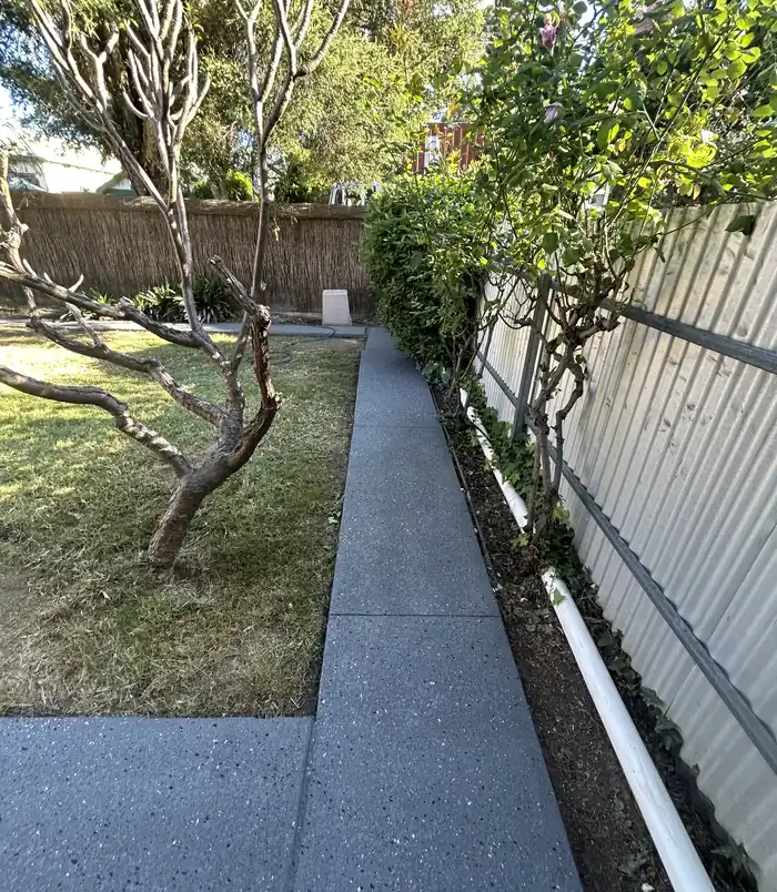 Dark grey resurfaced concrete path through a garden beside a metal fence