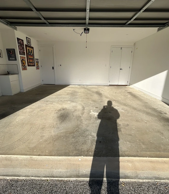 Stained, dusty concrete garage floor with framed memorabilia on the walls, before epoxy flooring