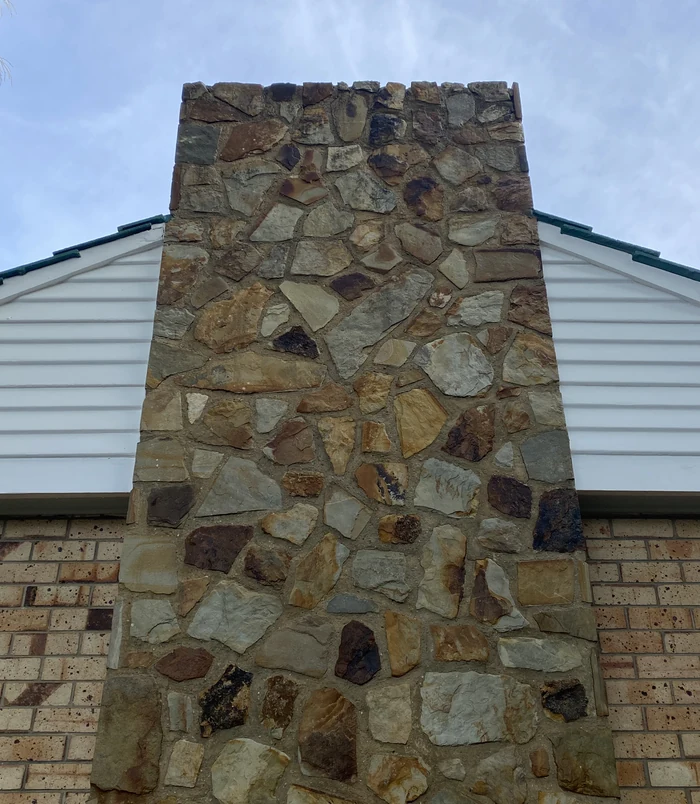 Clean natural stone chimney on a weatherboard house under a blue sky after pressure washing
