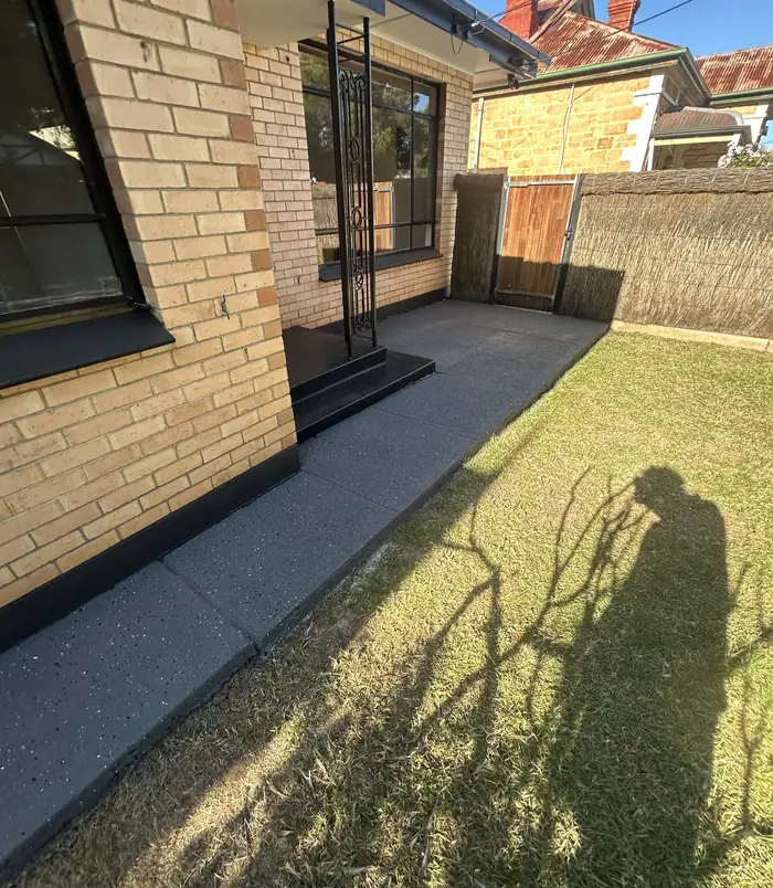 Dark grey resurfaced concrete patio beside a brick wall, sliding door and lawn