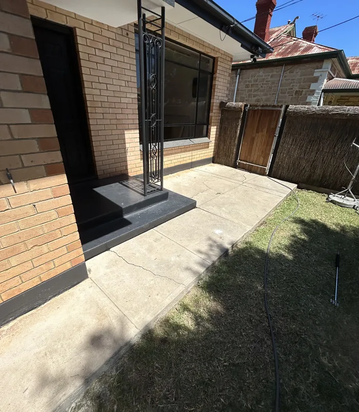 Worn concrete entry and path beside a brick wall and timber gate, before concrete resurfacing
