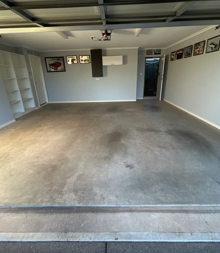 Dirty, oil-stained concrete floor in a garage with built-in shelving, before epoxy flooring