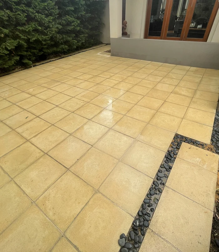 Clean, golden patterned paving in a backyard beside a house after pressure washing
