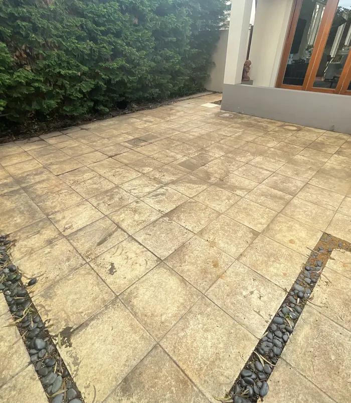 Dull, grimy patterned paving in a backyard beside a house, before pressure washing