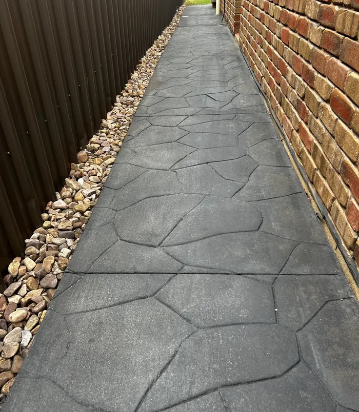 Narrow stamped concrete side path beside a brick wall and fence, before concrete resurfacing