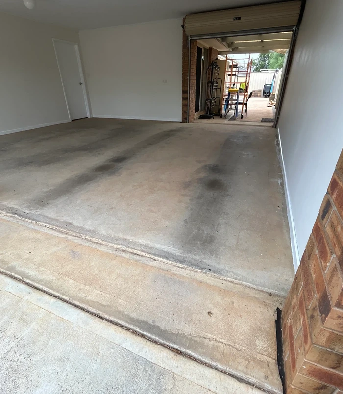 Dull, stained concrete garage floor beside a side door, before epoxy flooring