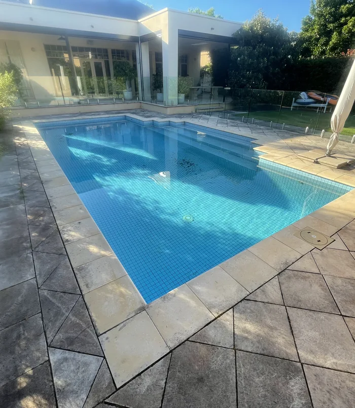 Dirty, dull pool surround and paving beside a blue swimming pool, before pressure washing