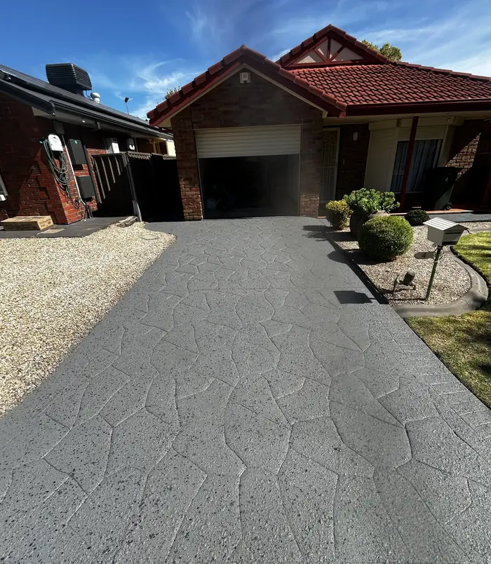 Dark grey resurfaced concrete driveway leading to a garage with a gravel garden