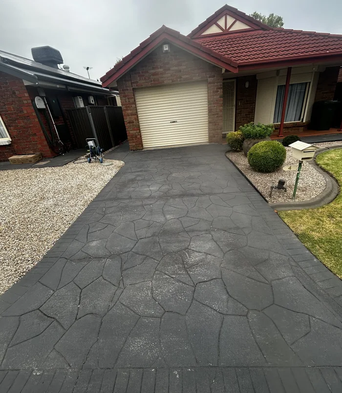 Worn concrete driveway leading to a garage with a cream door and gravel garden, before resurfacing
