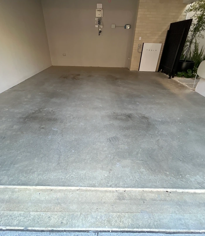 Bare, stained concrete garage floor in an empty double garage, before epoxy flooring