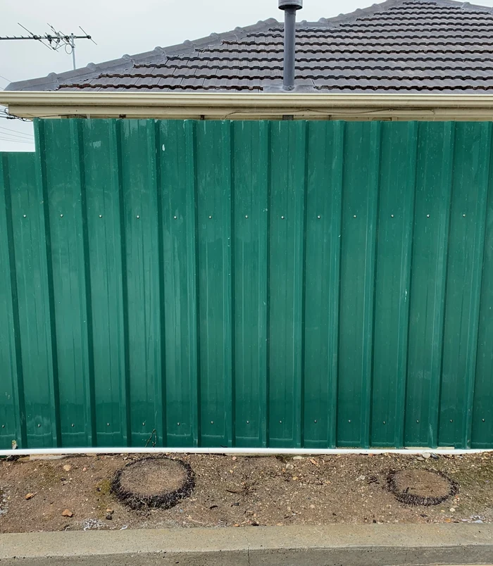 Clean, deep green metal fence beneath a tiled roof after pressure washing