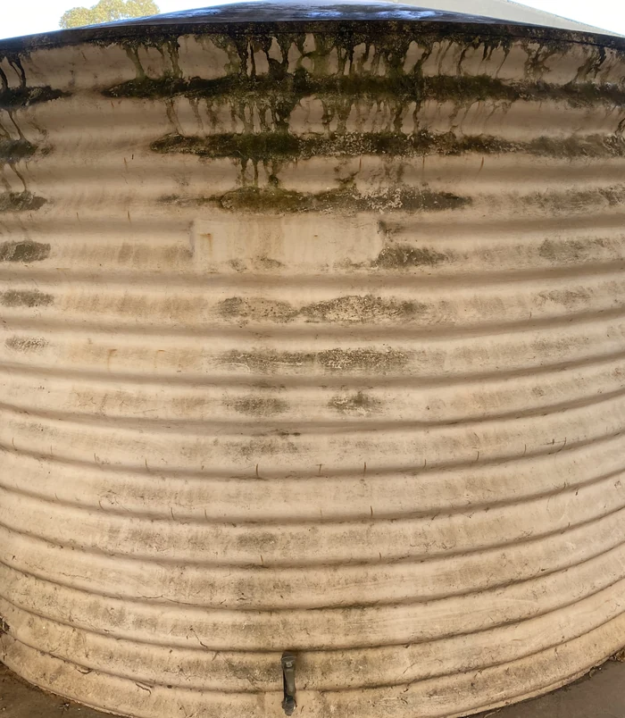 Corrugated water tank streaked with moss and grime near the top, before pressure washing