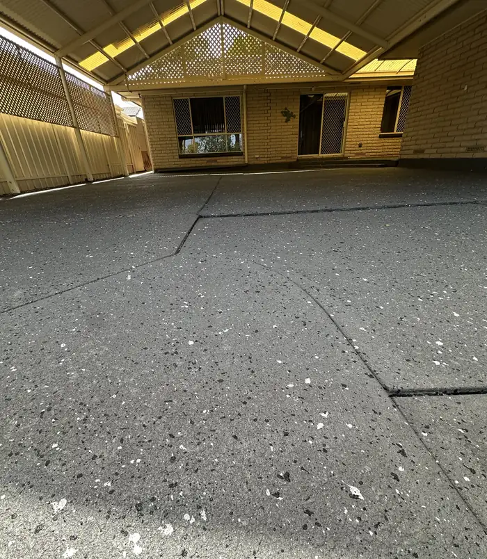 Dark grey resurfaced concrete floor under a pergola beside a brick home