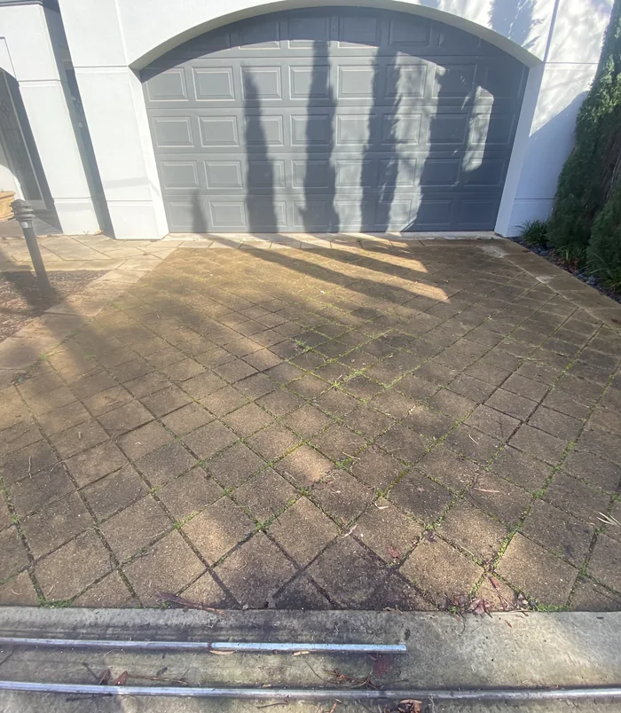 Stained, dirty concrete driveway in front of a grey garage door, before pressure washing
