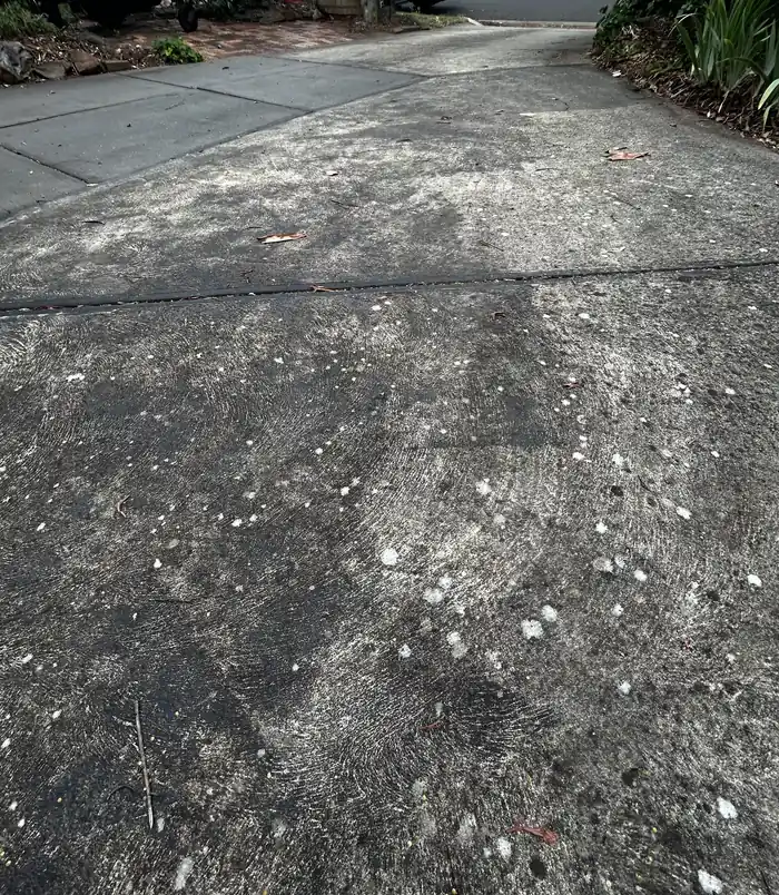 Stained, patchy concrete driveway with cracks and dirt, before concrete resurfacing